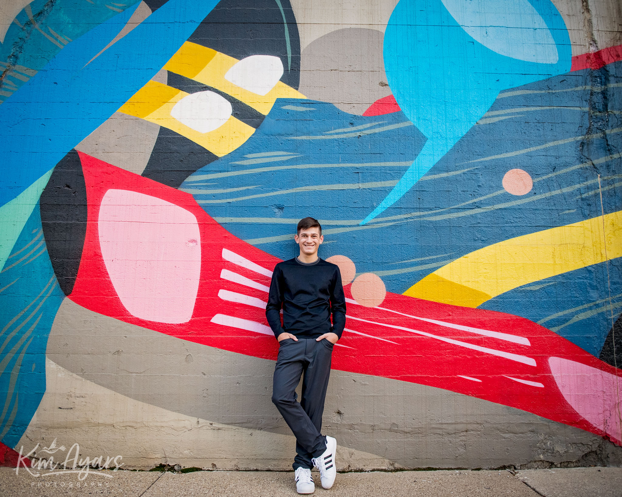 A high school senior stand agains a colorful mural in downtown Aurora.
