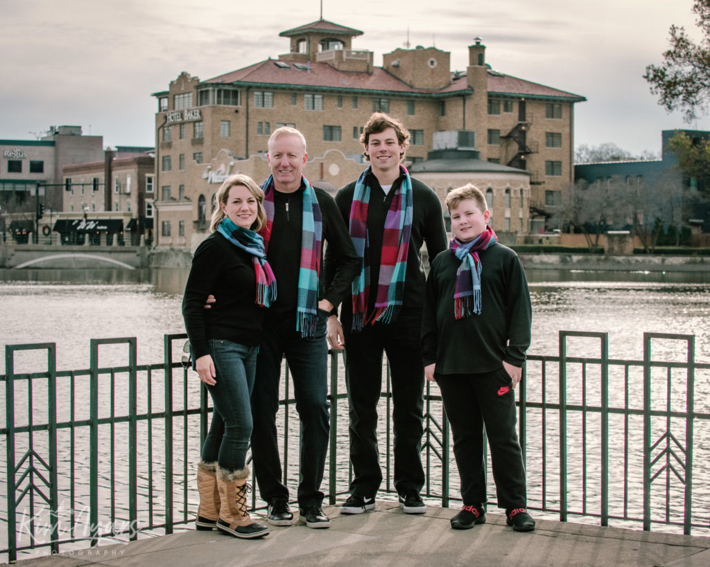 A family of four stands in front of the Fox River with Hotel Baker in the background.